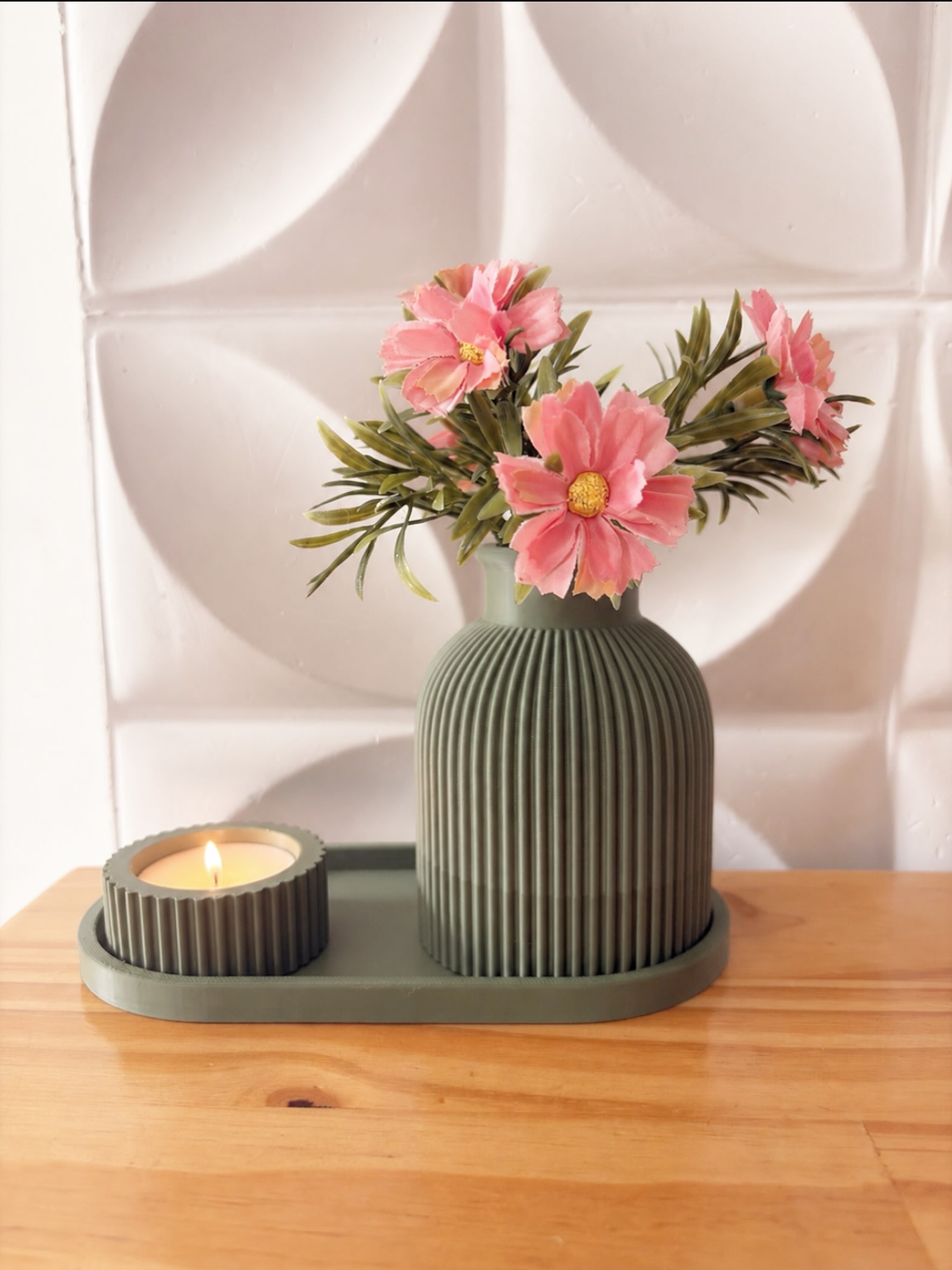 Vaso canelado verde impresso em 3D com flores, ao lado de porta-vela